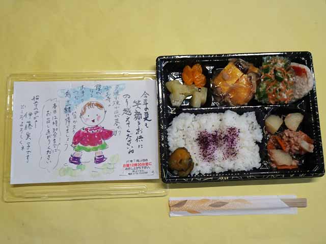 配食サービスの弁当、右側弁当、左側メッセージ。弁当は黒い弁当箱に収められ、左下から時計回りに、ゆかりご飯と漬物、みかんとパイナップルのシロップ漬け、卵焼きのきのこあんかけ、ハンバーグと夏野菜の和物、じゃがいもとツナの煮物。メッセージには、童謡「山寺」の一節と女の子の絵があしらわれている。